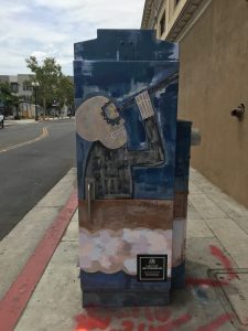 Utility box with art of a night scene with a skeleton-like creature looking at the moon through a monocular