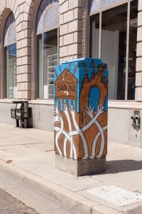 Utility box with art of santa ana landmarks and hands reaching toward the landmarks