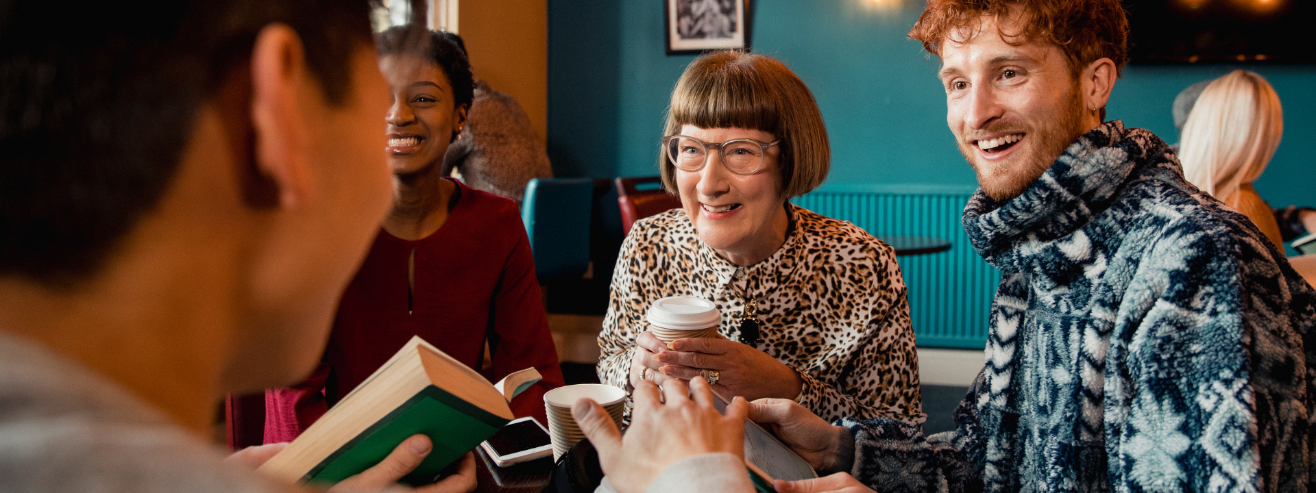 People in a discussion at a coffee shop with books and coffee cups