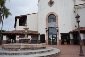 A train station entrance with white walls, red brick outdoor plaza and a fountain.