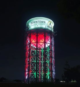 A water tower illuminated in white, red and green at night.