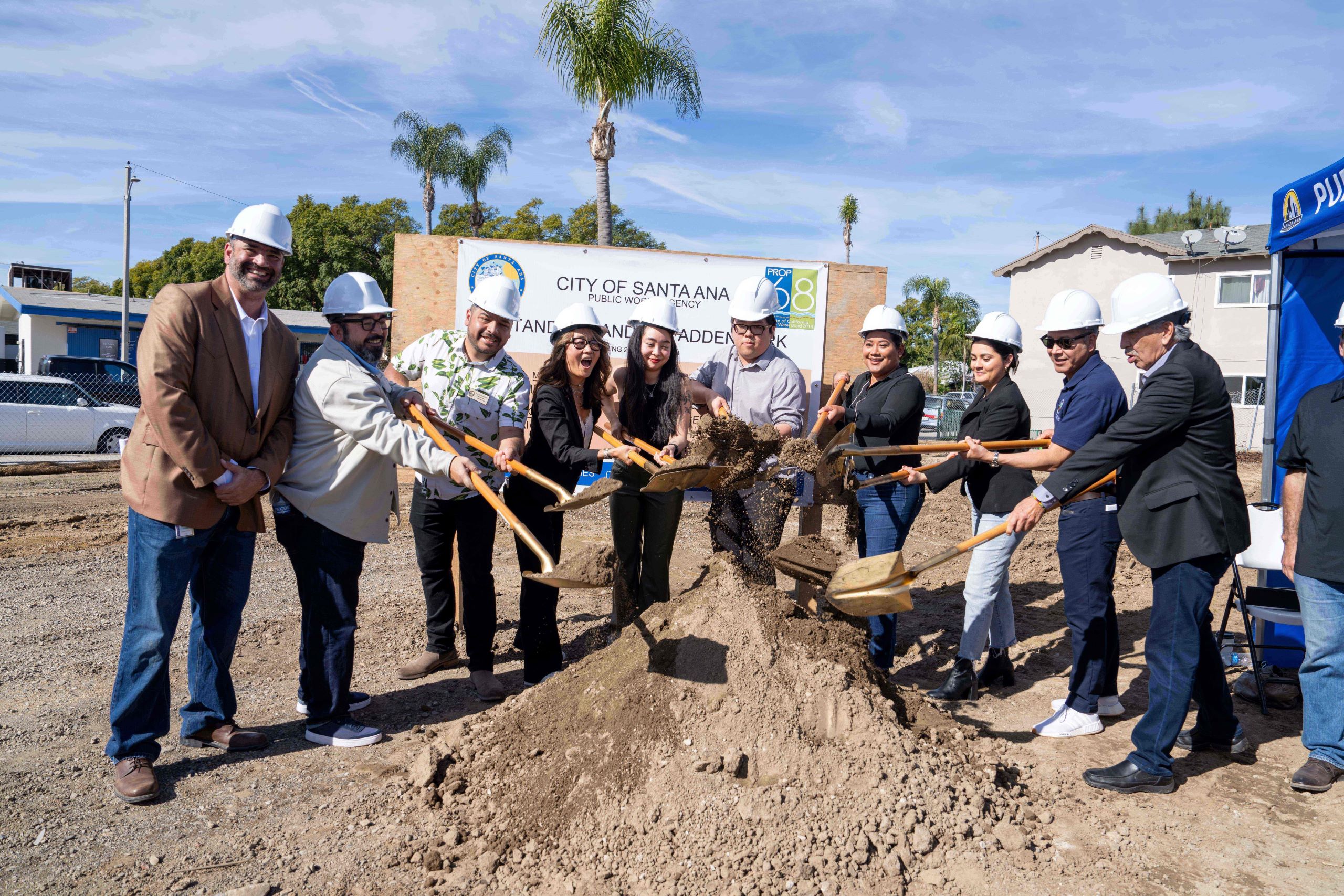 A group of people wearing hard hats use shovels to dig into a pile of dirt.