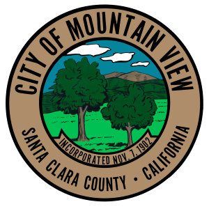 The Mountain View City seal is circular. In the middle there is an image of two trees with mountains and clouds in the background. The rim of the circular seal has lettering that reads "City of Mountain View" on top and "Santa Clara County - California" on the bottom of the circle.