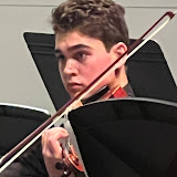 A young man playing a viola seated behind a music stand.