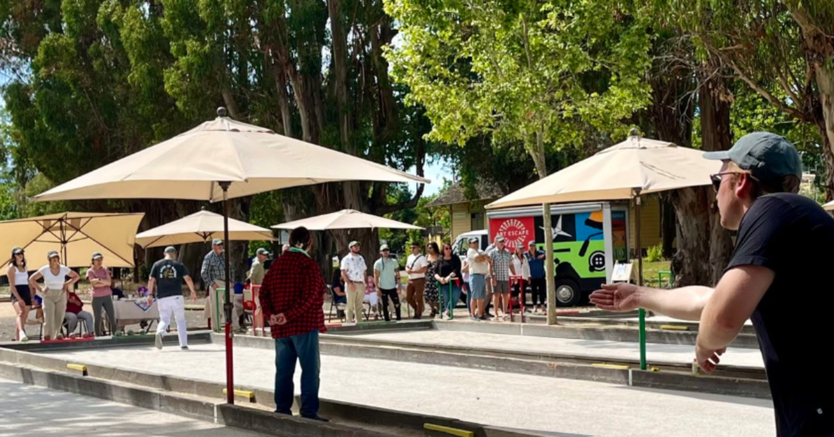 A man throwing a bocce ball with other players watching.