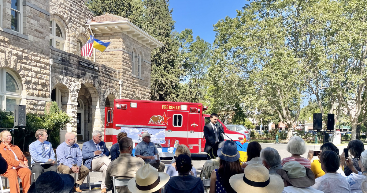 A photo of a man at a podium in front of an ambulance parked in front of Sonoma City Hall.