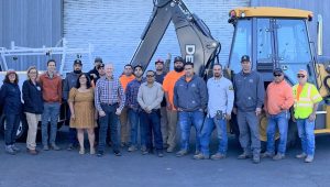 A group of people lined up in front of a pick up truck and backhoe.