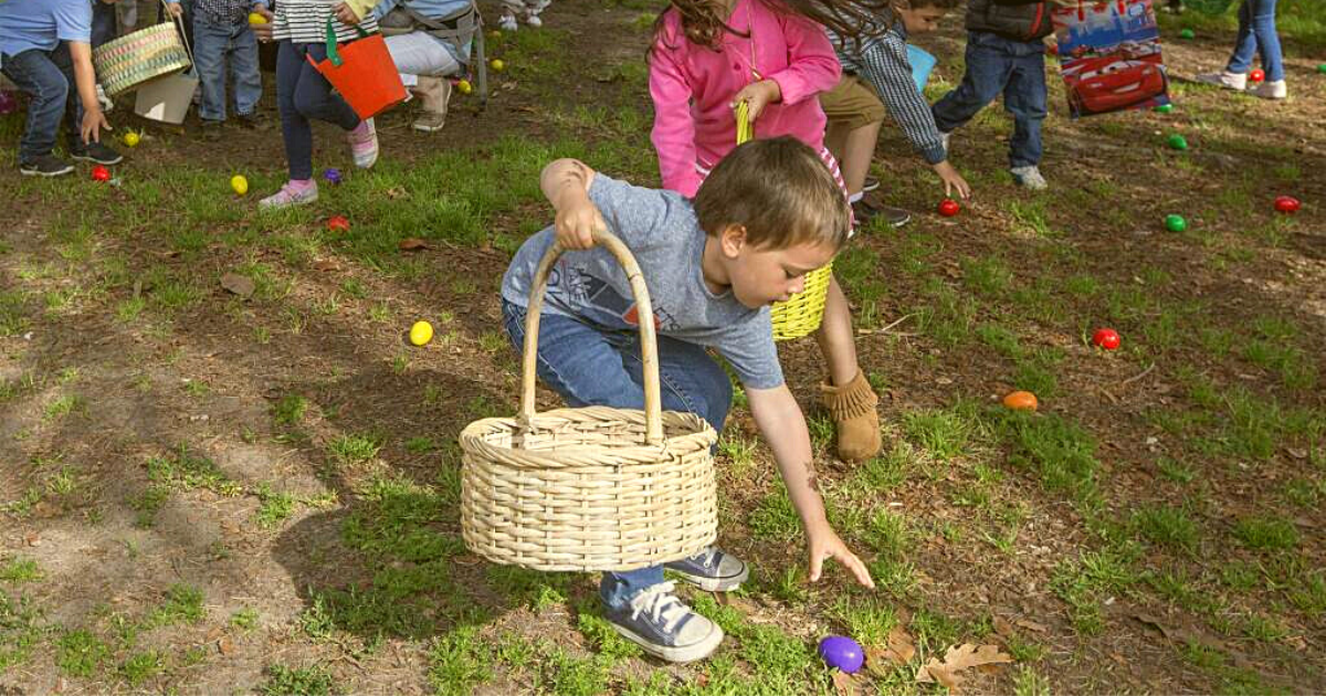 Children with baskets picking up colorful eggs from the grass.