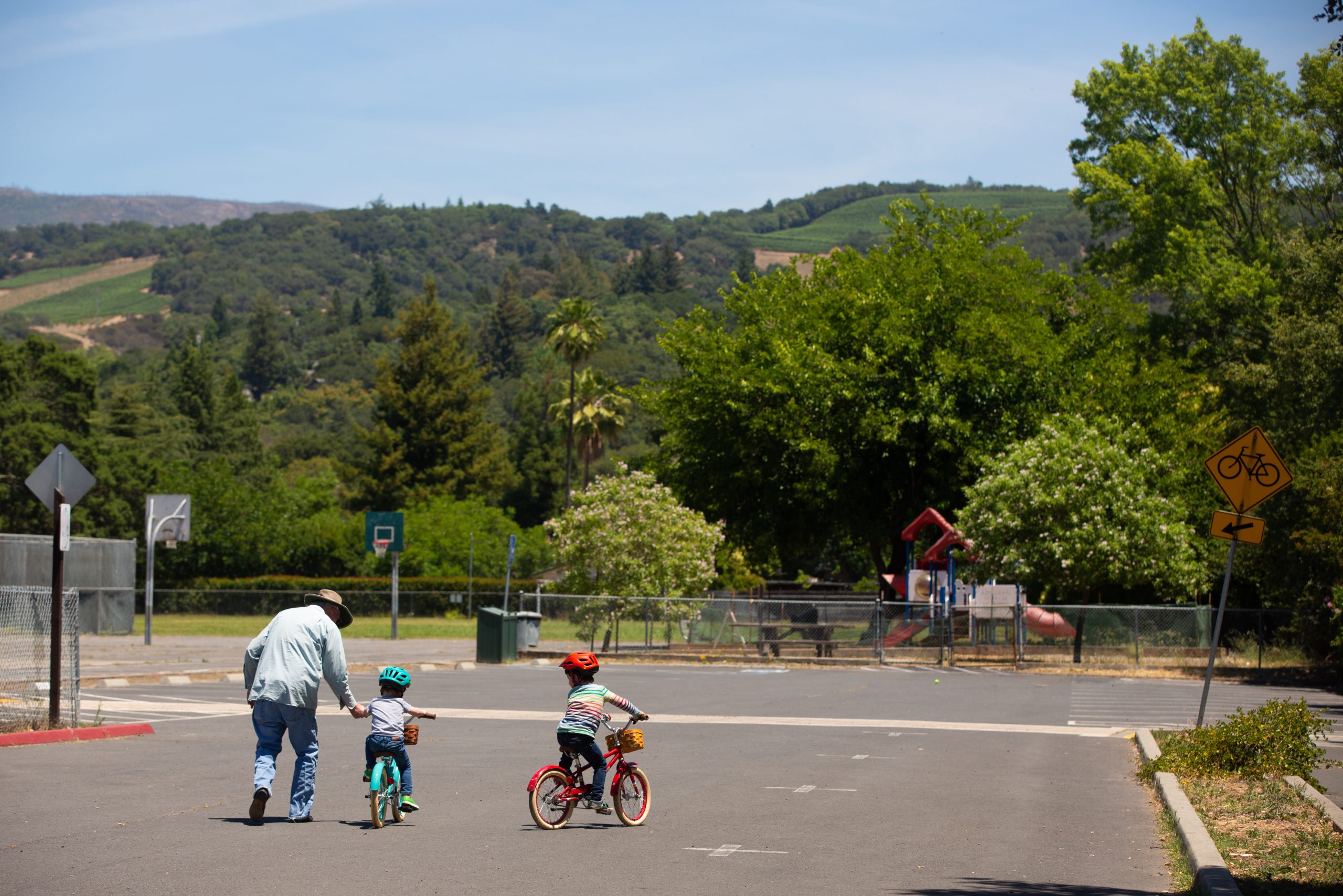 Kids learning to ride bikes on basketball court at a park.