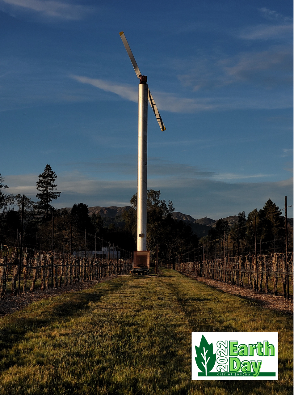 Photo of windmill in wine grape vineyard with trees and mountain in the distance.