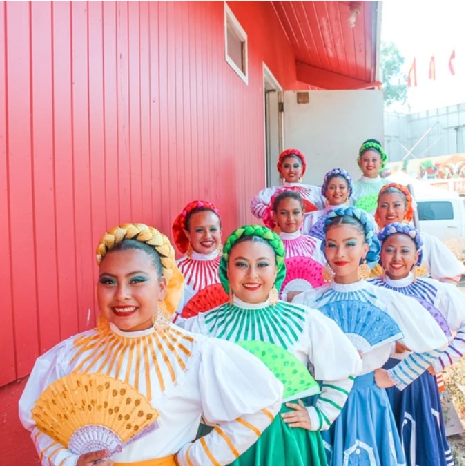 Group of women dressed in colorful costumes and holding fans.