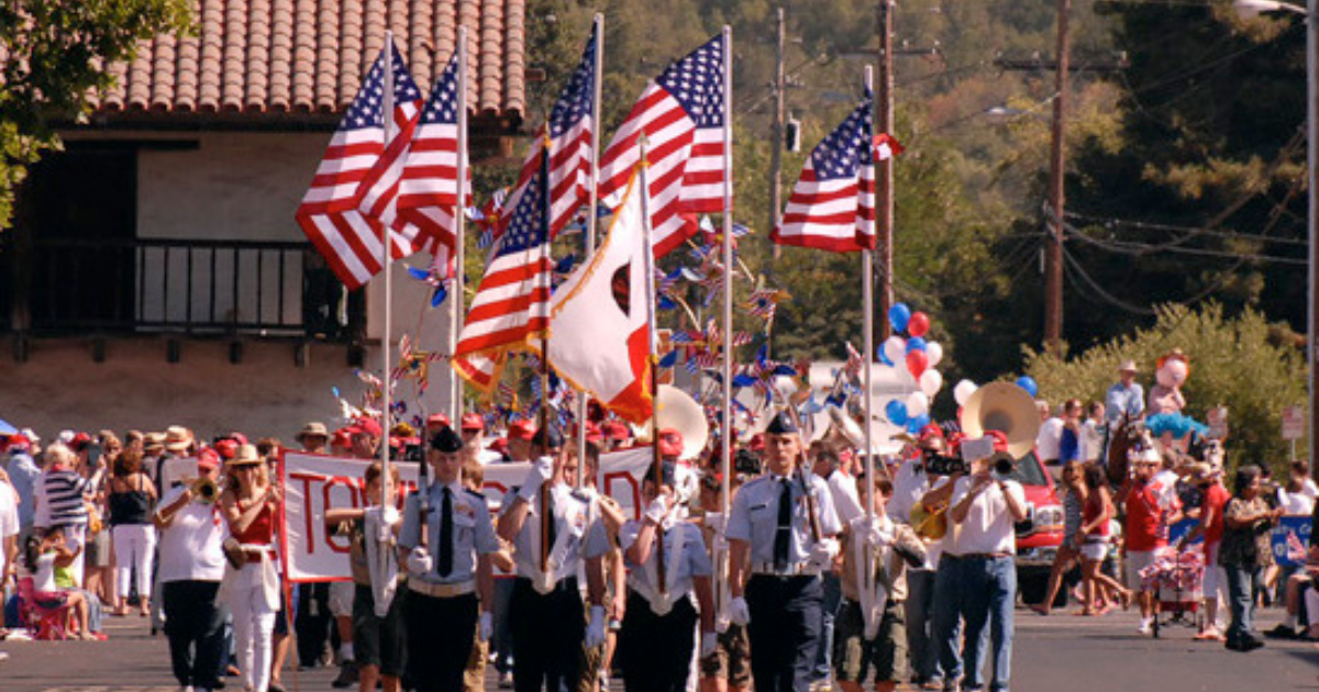 People marching in a parade holding American Flags.