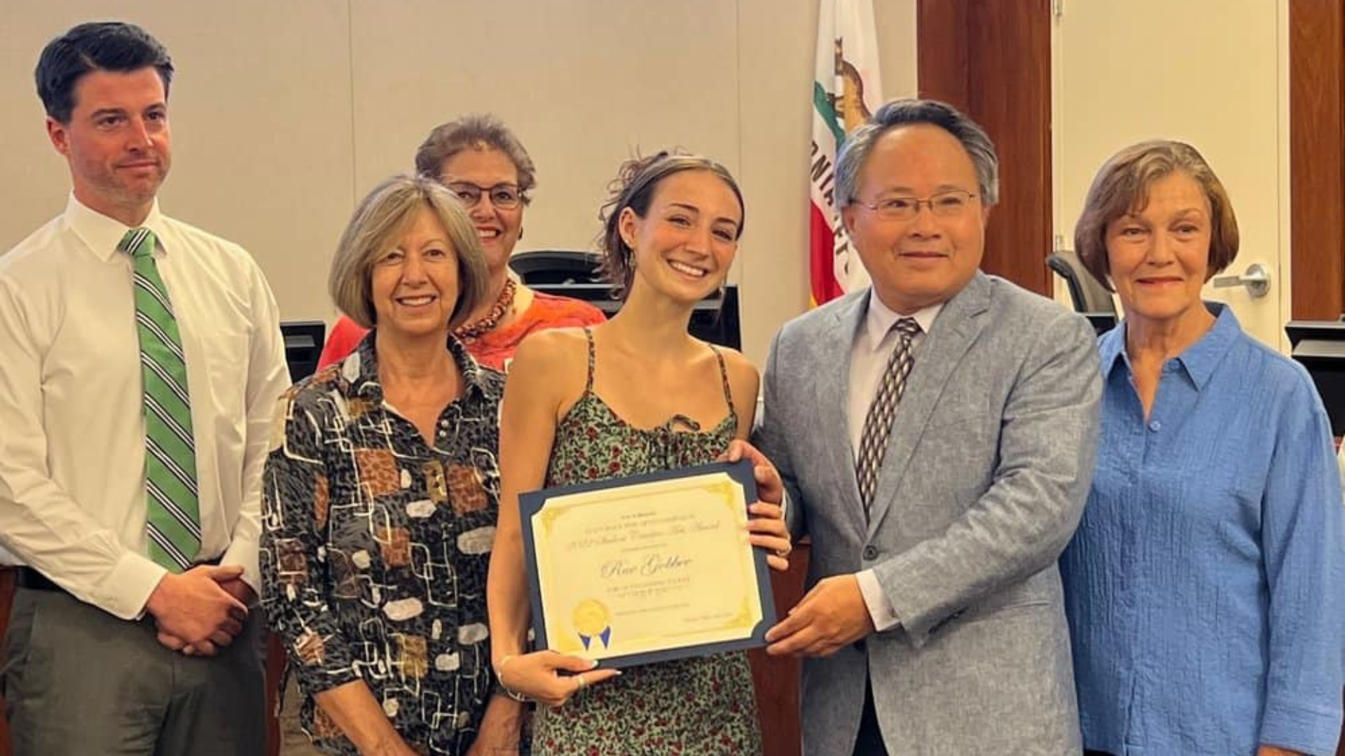 A man presenting a certificate to a woman with several people posing next to them.