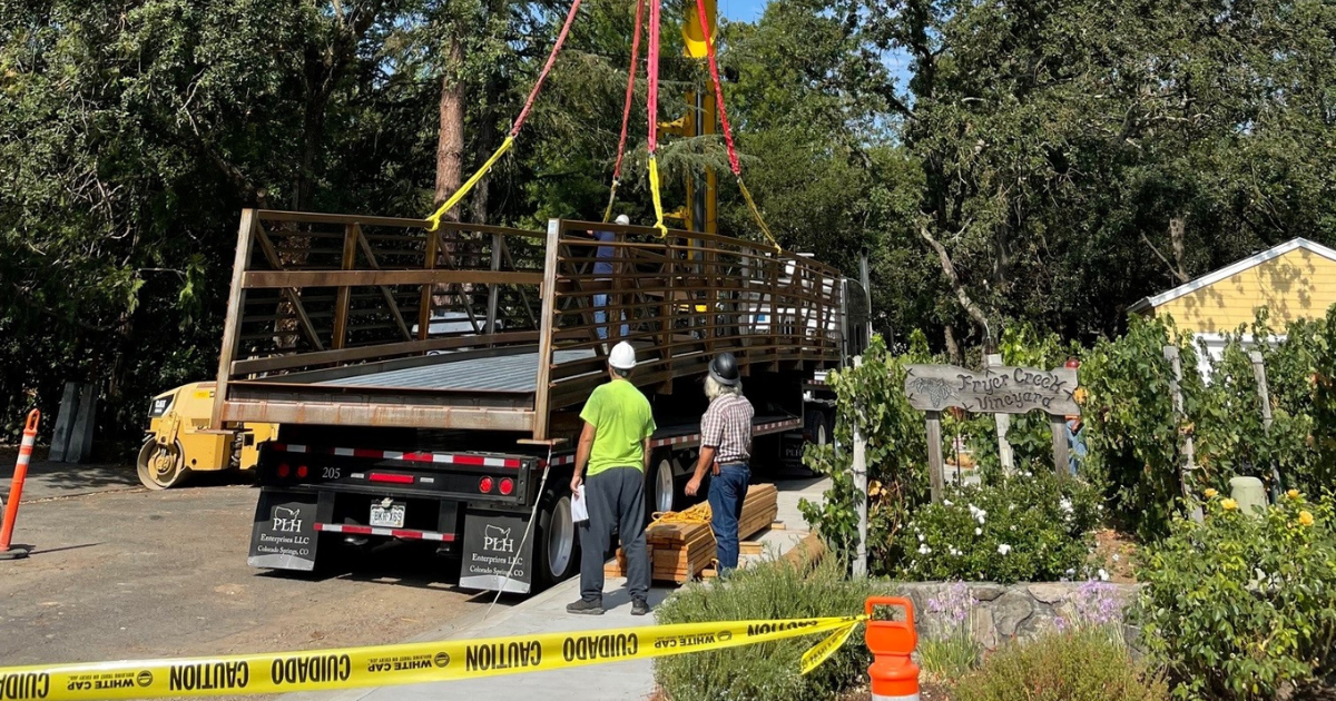 Two construction workers standing in front of a metal bridge attached to a crane on the flatbed of a truck.