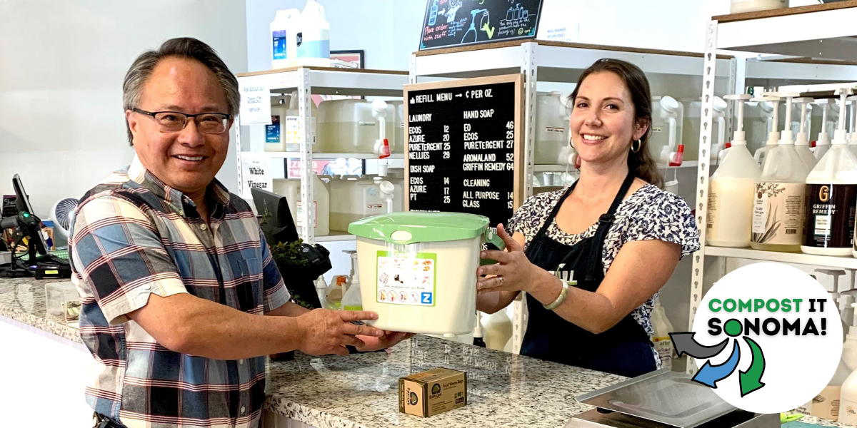 Woman handing a man a free compost pail over a counter in a store.