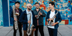 Four men standing in front of a colorful wall with instruments in thier hands.