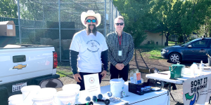 Two people standing in front of tables with water saving tools and compost pails.