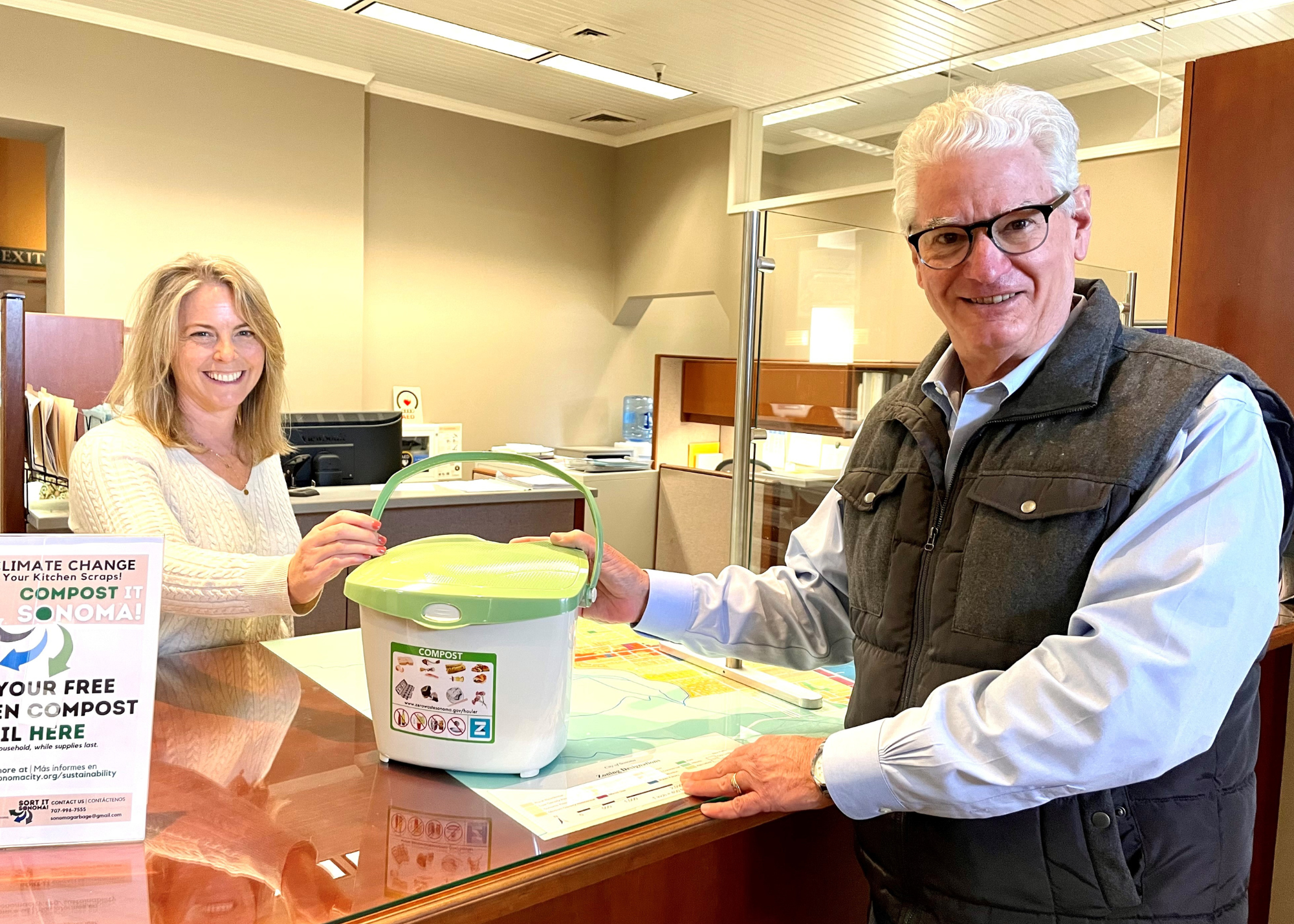 A woman handing a man a countertop compost pail over a counter.