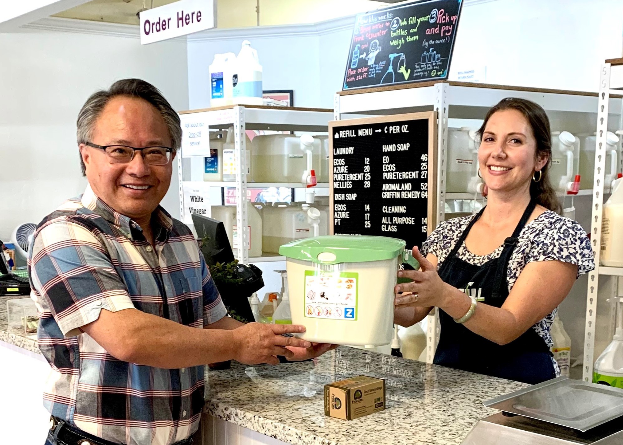 A woman handing a man a countertop compost pail.