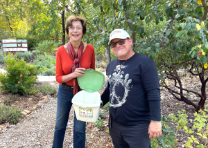 Man and woman holding a compost pail with the lid open in a park.