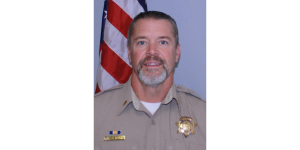 Photo of a man in a police officer uniform in front of an american flag.