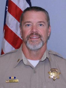 Photo of a man in a police officer uniform in front of an american flag.