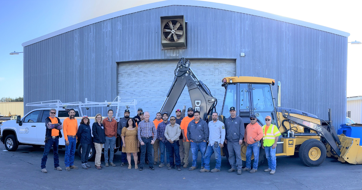 A photo of the public works staff in front of a work truck and backhoe.