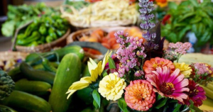 Photo of colorful flowers and fresh vegetables in bowls and baskets.