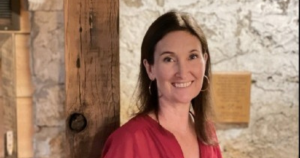 A woman wearing a red top leaning on a post and smiling with a rock wall in the background.