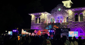 Sonoma City Hall at night with a stage and band playing and a crowd watching, the building is lit up in purple lights.