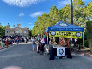 A pop tent with banners advertising a bike valet service with Sonoma City Hall in the background.