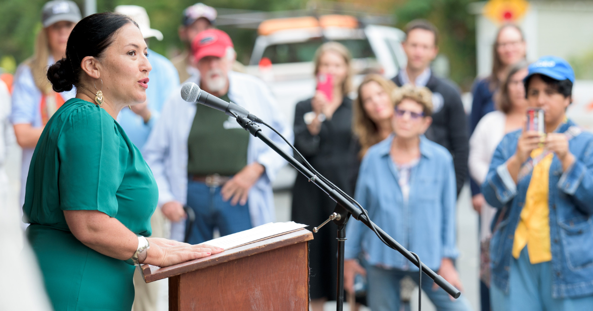 Ada Limon, 24th Poet Laureate of the United States, stands at a podium addressing a crowd during a bench dedication ceremony on August 18, 2023.