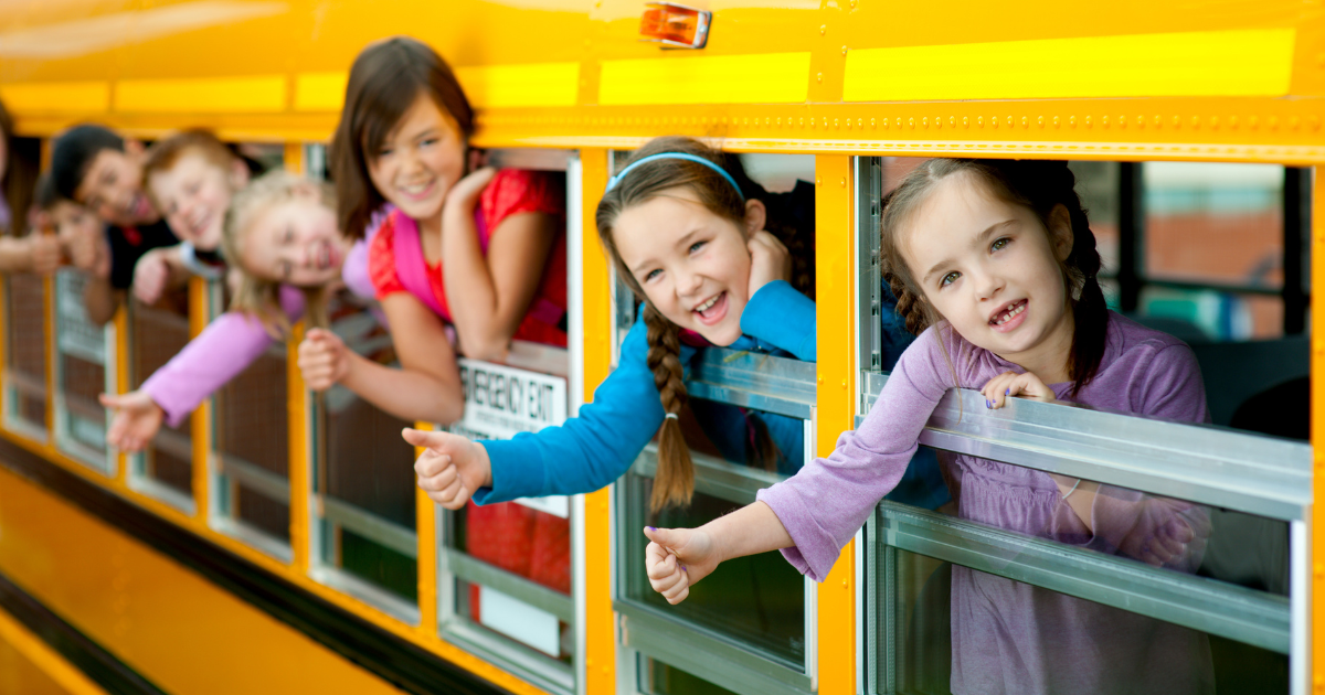 Kids giving a 'thumbs up' from the windows of a school bus.