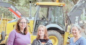 Three people in front of a backhoe.