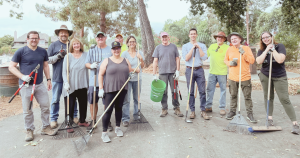 a group of people standing together and holding yard tools.