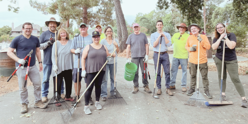 a group of people standing together and holding yard tools.