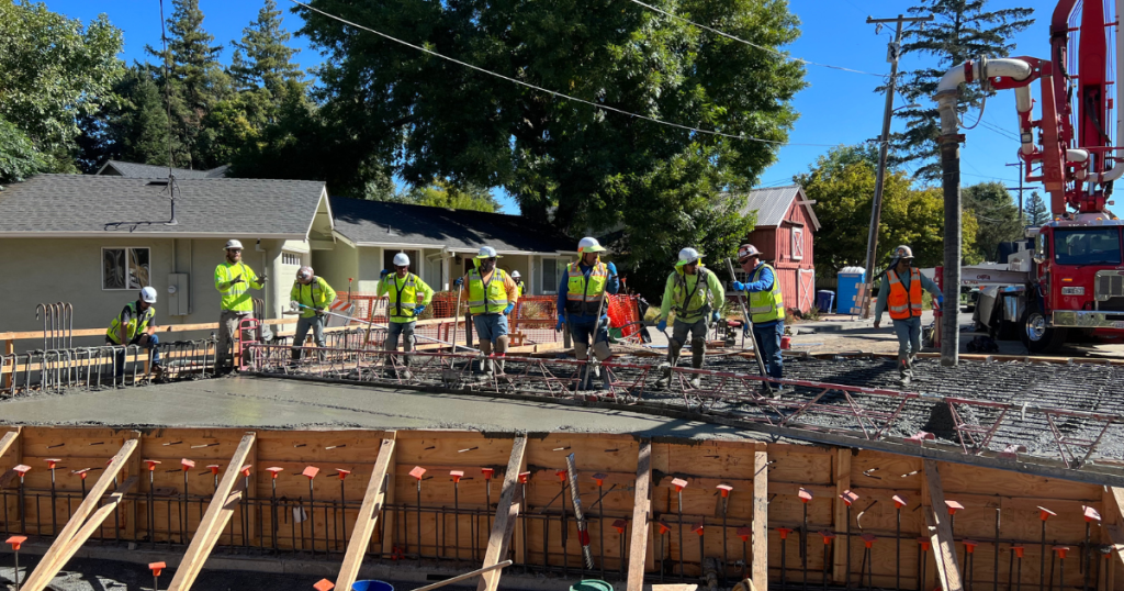 A photo of a row of workers smoothing concrete being poured on the deck of a new bridge.