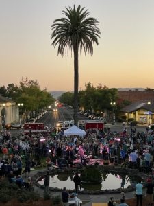 Photo of a park with a band and crowd of people at sunset from a distance.