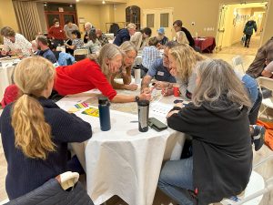 A group of people sitting around a table and making notes on a map in the center of the table.