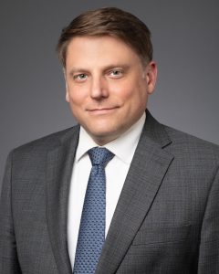 Portrait of a man in a gray suit and blue tie.