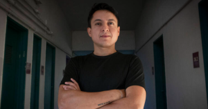 A photo of a man in black shirt in a hallway with his arms crossed.