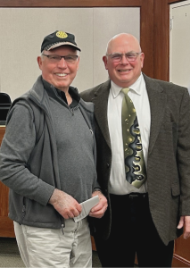 A photo of two men standing beside eachother and smiling at the camera.