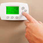 A person's hand on the down arrow button of a digital thermostat.