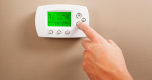 A person's hand on the down arrow button of a digital thermostat.