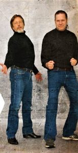 Two men in black turtleneck sweaters and jeans standing