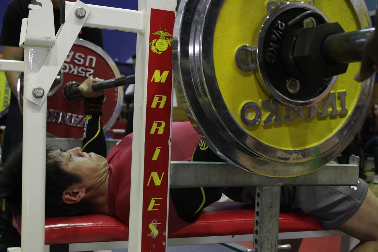 Lifter performing a heavy barbell bench press in a gym power rack