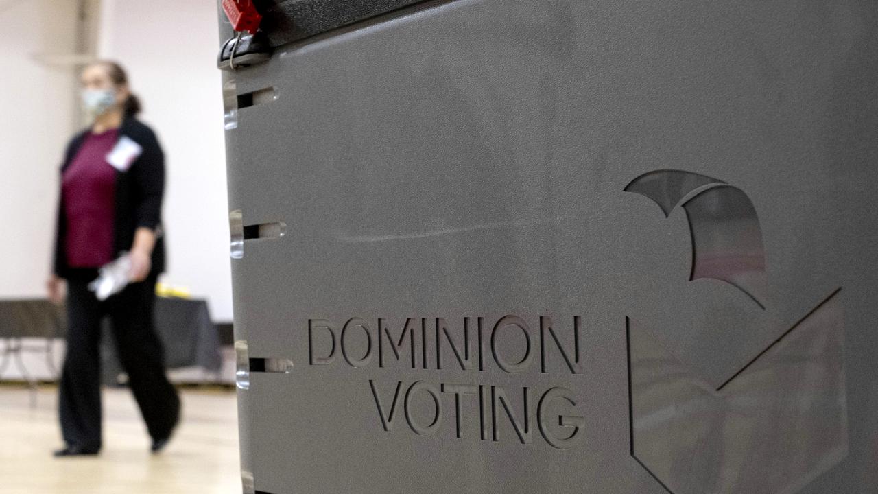 A worker passes a Dominion Voting ballot scanner.
