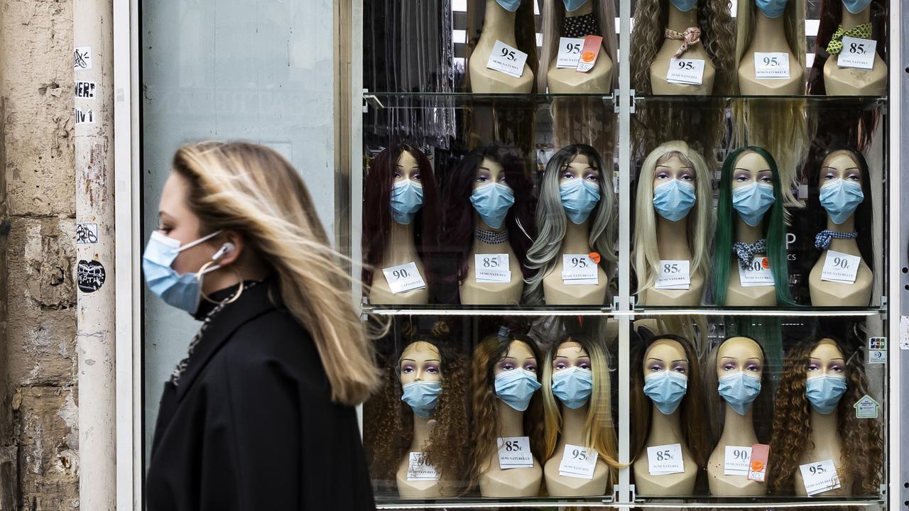 A woman wearing a face mask walks past a shop displaying masks