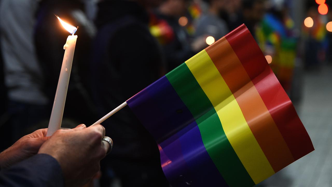 A person holds a candle and a rainbow flag