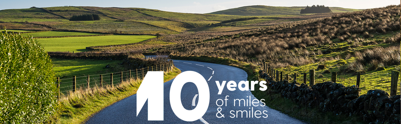 Text that reads '10 years of miles & smiles' at the forefront of an image that shows a country road and surrounding scenery